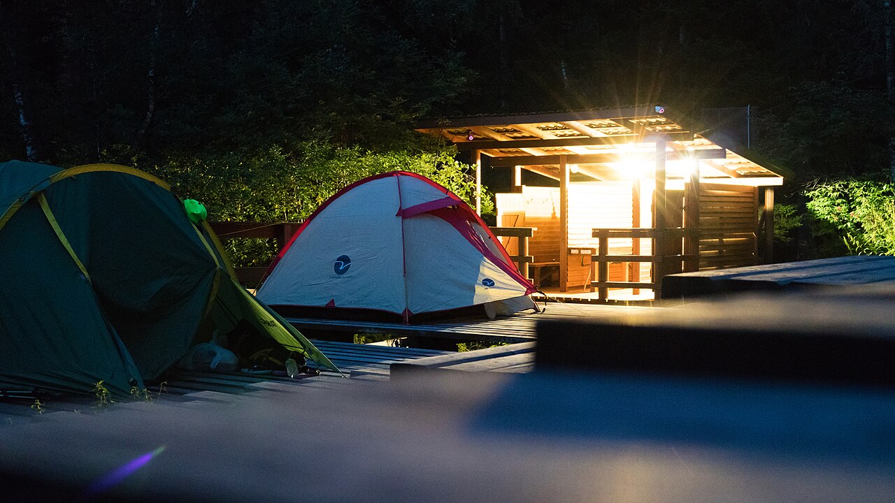 tentes de camping dans l'obscurité, sans lumière propre, un bâtiment éclairé au loin en arrière-plan