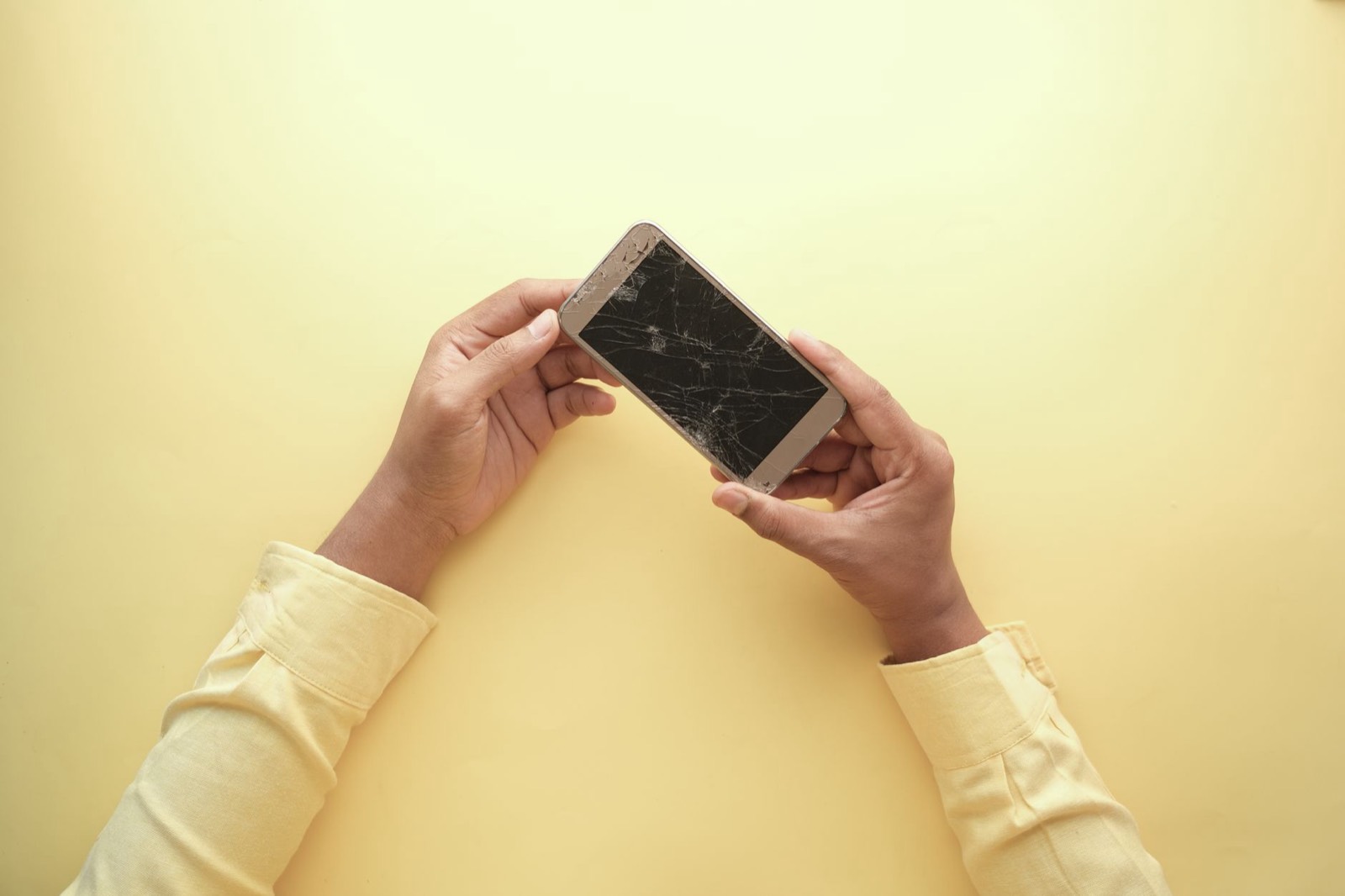 Main tenant un smartphone dont l'écran est fissuré