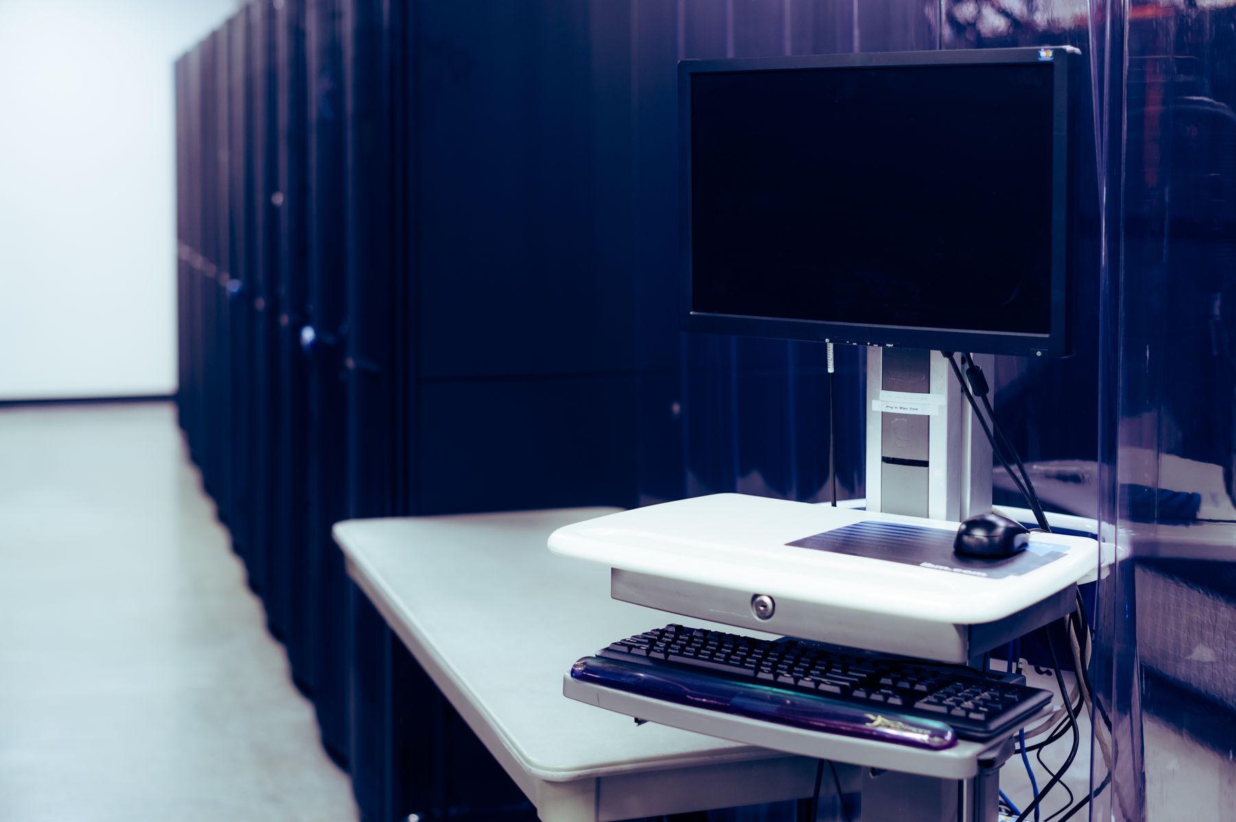 Poste de console avec écran et clavier installé devant une rangée de baies de serveurs dans un centre de données